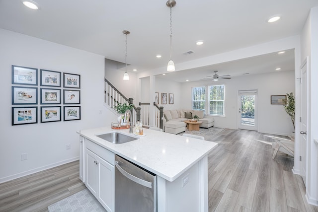 kitchen with decorative light fixtures, stainless steel dishwasher, sink, white cabinetry, and an island with sink