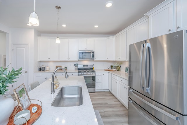 kitchen featuring appliances with stainless steel finishes, pendant lighting, white cabinets, light stone counters, and sink