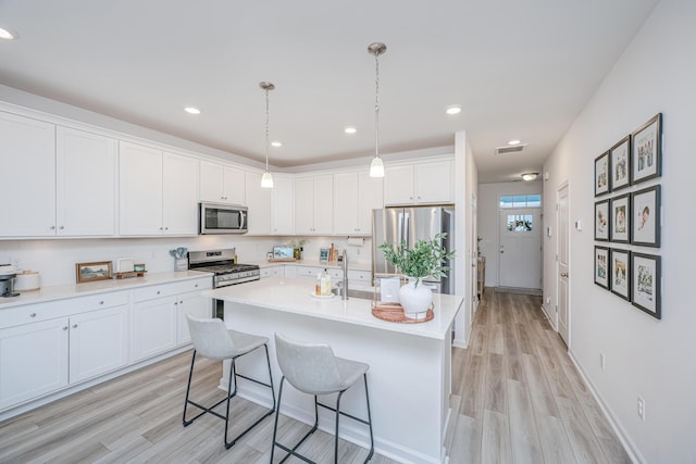 kitchen with white cabinets, appliances with stainless steel finishes, hanging light fixtures, a breakfast bar, and a center island with sink