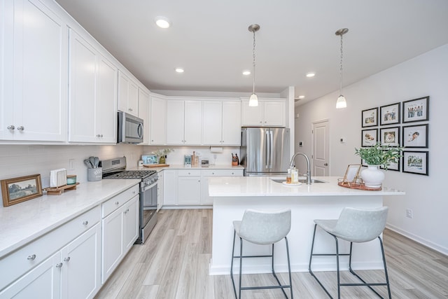 kitchen featuring white cabinets, appliances with stainless steel finishes, decorative light fixtures, light hardwood / wood-style floors, and sink