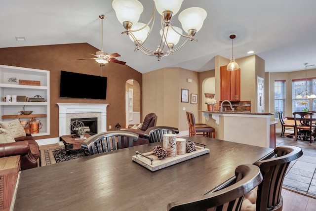 dining space featuring built in shelves, light hardwood / wood-style floors, ceiling fan with notable chandelier, and vaulted ceiling