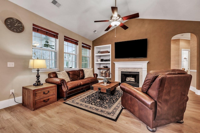 living room with a premium fireplace, built in shelves, ceiling fan, and light hardwood / wood-style flooring