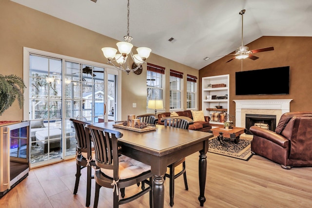 dining area featuring ceiling fan with notable chandelier, built in shelves, a premium fireplace, wine cooler, and vaulted ceiling