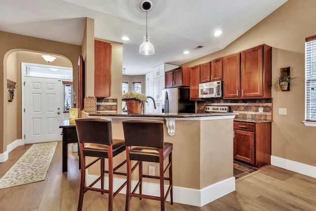 kitchen with a kitchen bar, appliances with stainless steel finishes, decorative backsplash, light hardwood / wood-style flooring, and kitchen peninsula