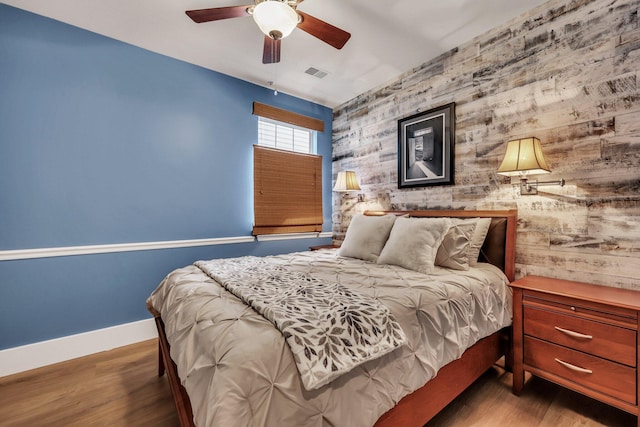 bedroom featuring ceiling fan, dark hardwood / wood-style flooring, and wooden walls