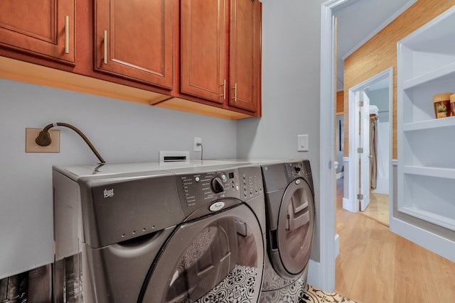 laundry area featuring washing machine and clothes dryer, light hardwood / wood-style floors, and cabinets