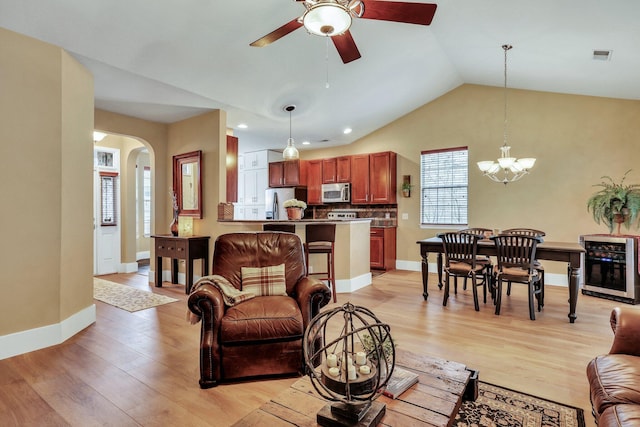 living room with vaulted ceiling, ceiling fan with notable chandelier, light hardwood / wood-style floors, and beverage cooler