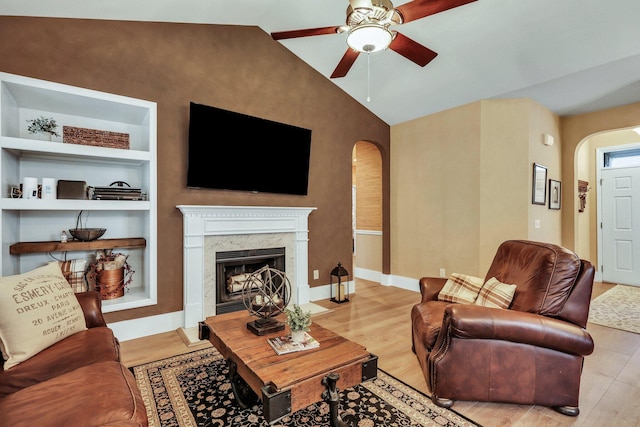 living room featuring light hardwood / wood-style flooring, ceiling fan, a high end fireplace, built in features, and lofted ceiling