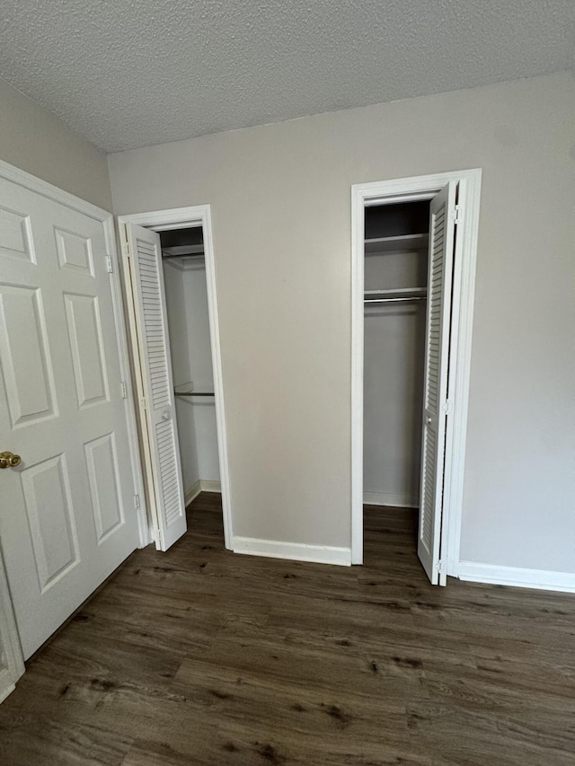 unfurnished bedroom with a textured ceiling, dark wood-type flooring, and two closets