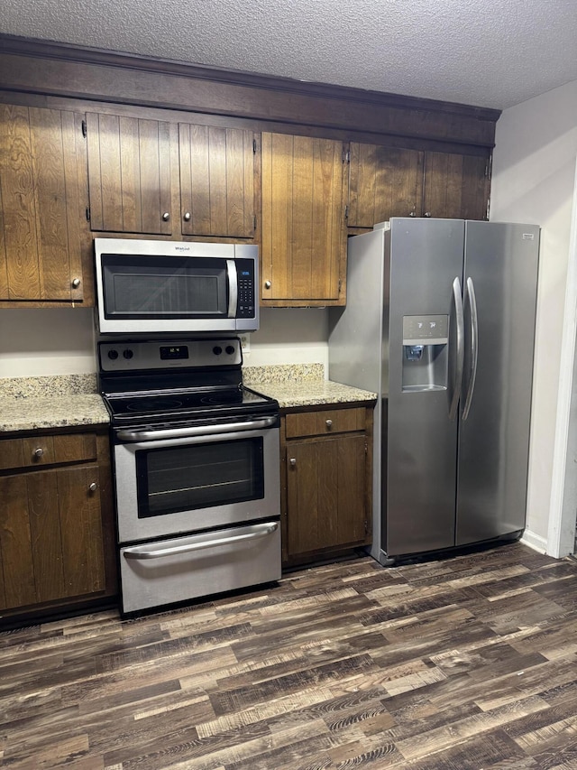 kitchen featuring light stone counters, dark hardwood / wood-style flooring, a textured ceiling, and appliances with stainless steel finishes