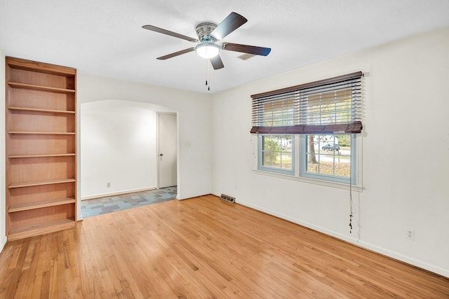 empty room featuring arched walkways, light wood-style floors, visible vents, and baseboards