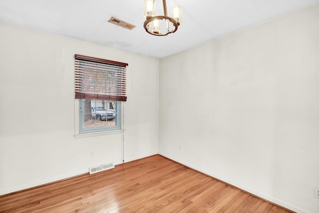 unfurnished room featuring light wood finished floors, visible vents, and a notable chandelier