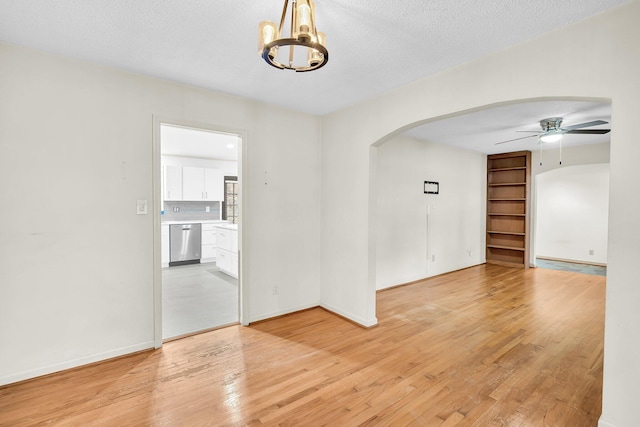 spare room with arched walkways, a textured ceiling, light wood-type flooring, and ceiling fan with notable chandelier