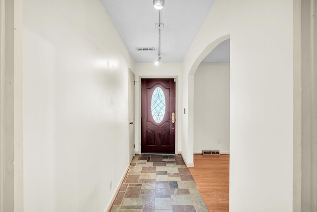 entryway featuring arched walkways, rail lighting, visible vents, and baseboards