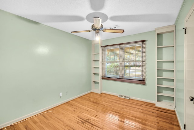 unfurnished room featuring wood finished floors, visible vents, baseboards, a textured ceiling, and ceiling fan