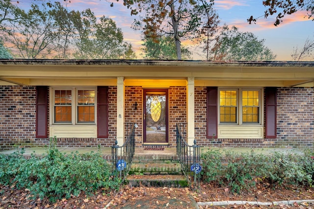 property entrance with brick siding, a porch, and fence