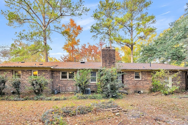 back of house featuring a chimney, central AC unit, and brick siding