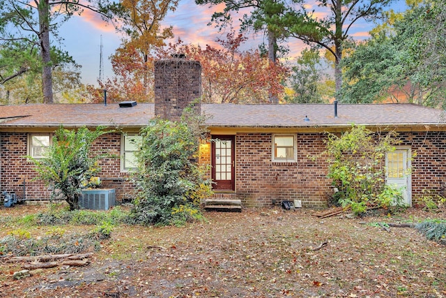 back of property at dusk with a chimney, brick siding, and central AC