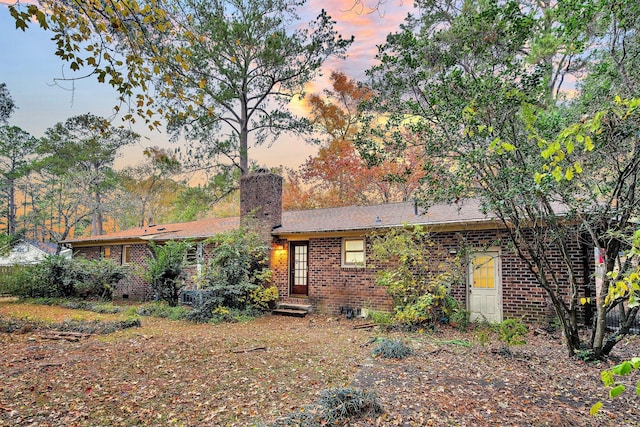 back of house at dusk with a chimney and brick siding