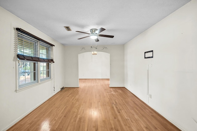 empty room with visible vents, a ceiling fan, arched walkways, light wood-type flooring, and baseboards