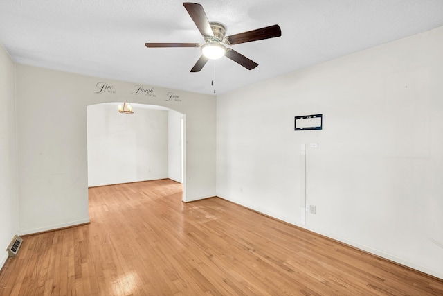 unfurnished room featuring ceiling fan, arched walkways, light wood-style flooring, baseboards, and visible vents
