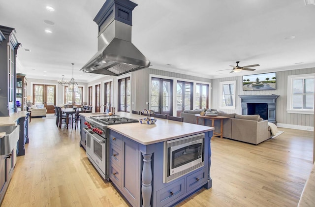 kitchen featuring island range hood, decorative light fixtures, stainless steel appliances, light hardwood / wood-style flooring, and a kitchen island with sink