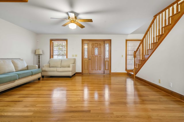 unfurnished living room with stairway, baseboards, a ceiling fan, and light wood finished floors