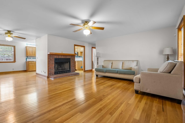 living area featuring ceiling fan, a fireplace, baseboards, and light wood-style floors