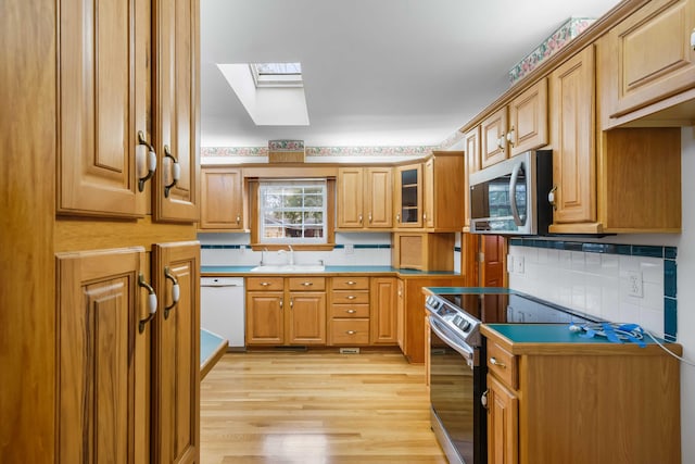 kitchen featuring a sink, tasteful backsplash, stainless steel appliances, a skylight, and light wood finished floors