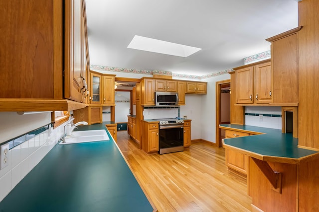 kitchen with a peninsula, a skylight, a sink, stainless steel appliances, and light wood-style floors