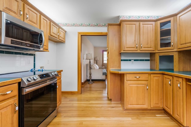 kitchen with baseboards, light wood finished floors, stainless steel appliances, decorative backsplash, and glass insert cabinets