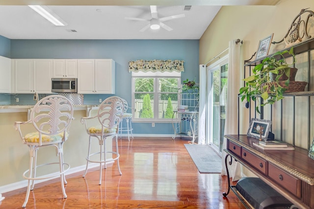 5406 E Crosland Ct, North Charleston, SC 29420 - kitchen featuring stainless steel microwave, light wood-type flooring, a breakfast bar area, white cabinetry, and a ceiling fan