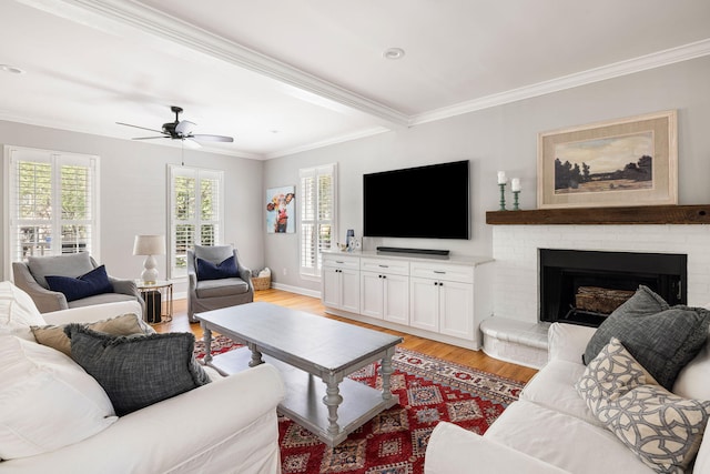 living area featuring ceiling fan, a brick fireplace, light wood-type flooring, baseboards, and ornamental molding