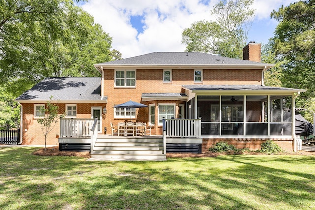 back of property with brick siding, a wooden deck, a sunroom, a chimney, and a lawn