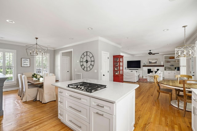 kitchen with light wood finished floors, ceiling fan with notable chandelier, white cabinetry, stainless steel gas stovetop, and ornamental molding