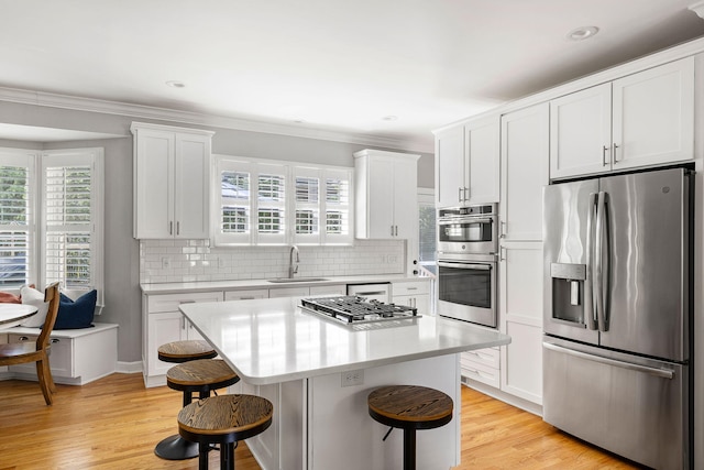 kitchen with appliances with stainless steel finishes, a sink, light countertops, white cabinets, and a breakfast bar