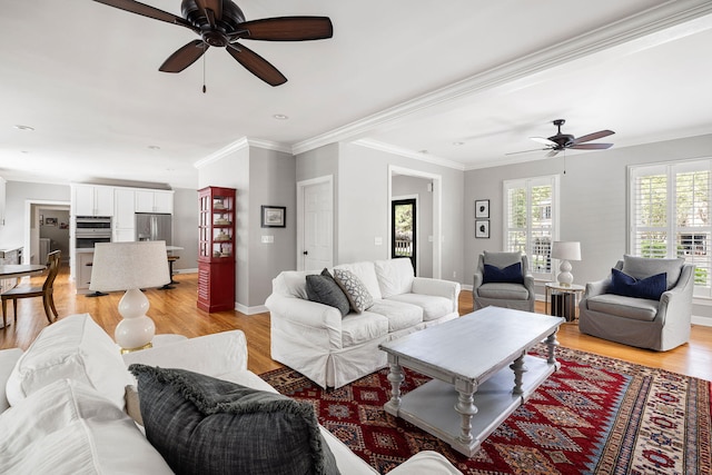 living room with crown molding, ceiling fan, baseboards, and light wood finished floors