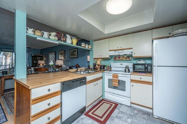 kitchen with sink, a raised ceiling, kitchen peninsula, white appliances, and white cabinets