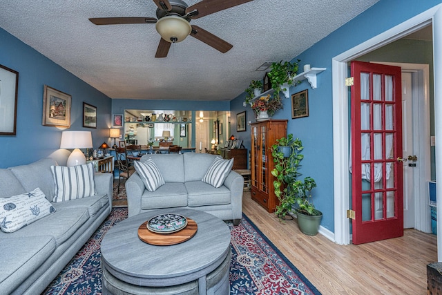 living room featuring ceiling fan, light hardwood / wood-style flooring, and a textured ceiling