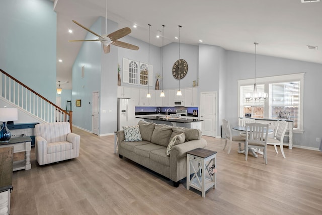 living area featuring light wood finished floors, stairs, visible vents, and ceiling fan with notable chandelier