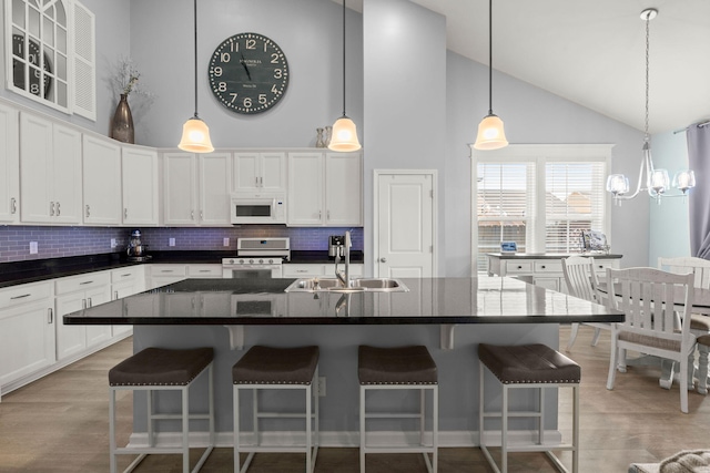 kitchen with white microwave, gas range, light wood-type flooring, white cabinetry, and a sink