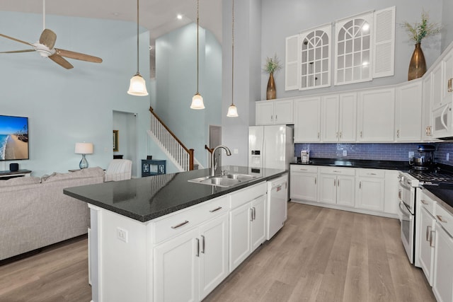 kitchen with white appliances, a towering ceiling, open floor plan, light wood-type flooring, and a sink