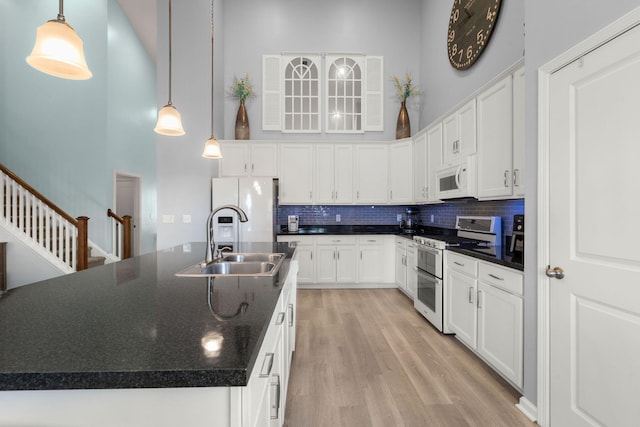 kitchen with white appliances, dark countertops, a sink, and a towering ceiling