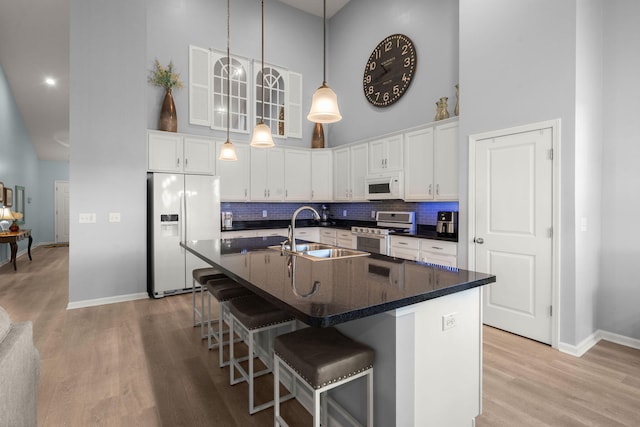 kitchen with white appliances, a high ceiling, a sink, light wood-type flooring, and dark countertops