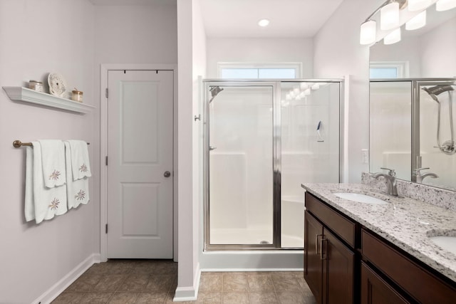 full bathroom featuring a stall shower, a sink, baseboards, and double vanity