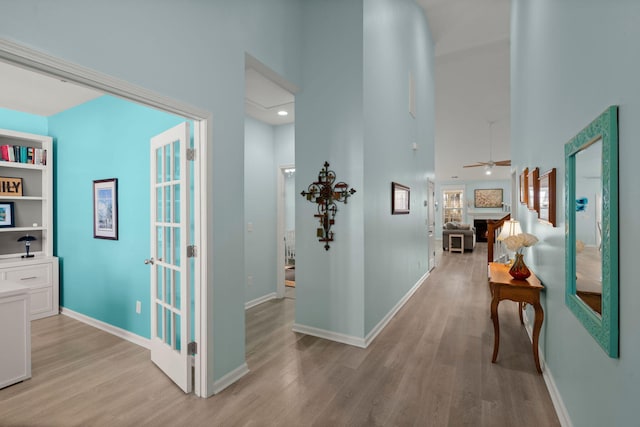 hallway with baseboards, a towering ceiling, and light wood finished floors