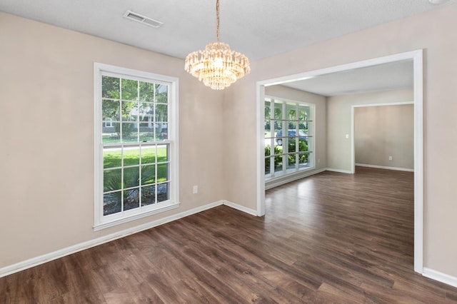 empty room with dark wood-style flooring, visible vents, and baseboards