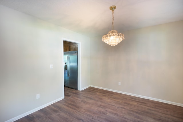 spare room with dark wood-style floors, baseboards, and a chandelier