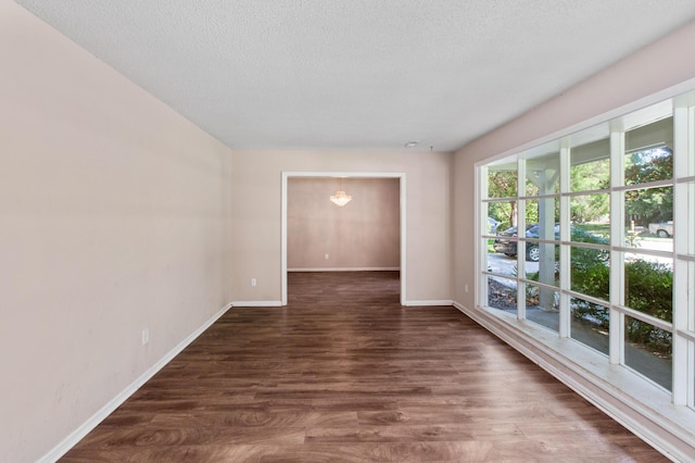 empty room featuring a textured ceiling, baseboards, and dark wood-style flooring