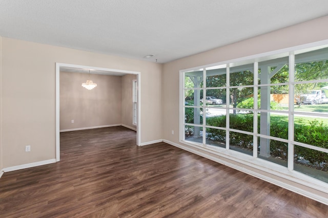 empty room with baseboards, dark wood-style flooring, a textured ceiling, and a notable chandelier